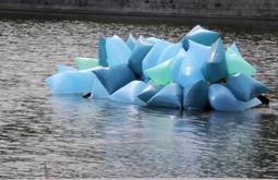 A small boat covered in large blue balloons floats along an inner city river.