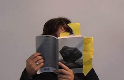 A person holds a book close while they read, yellow book marks stick out at various angles.