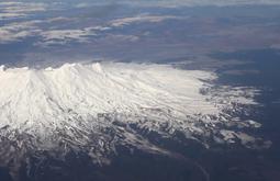 A snowy mountain and the surrounding environment is seen from a plane.