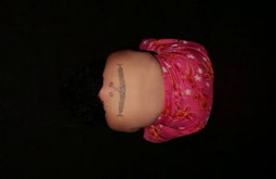 Surrounded by darkness a persons back is exposed while they bend over, a tattoo is centred between their shoulders.