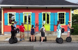 A group of people stand on Segway's outside a colourful house in New Orleans.