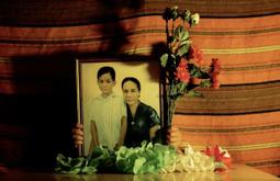 A portrait of a woman and a young boy sit on a table surrounded by artificial flowers