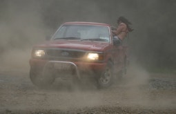 A red ute does a burn out on a gravel road as a person wearing devil wings hangs out the passenger door.