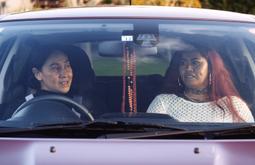 Two Pasifika women sit in a car, as if in conversation. The woman at left is the artist Edith Amituanai and at right the subject of the film, Epifania.