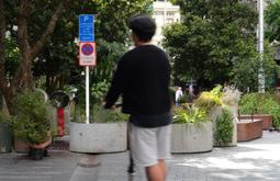A person rides through a public square on an escooter. The square is abundant with potted plants and trees.