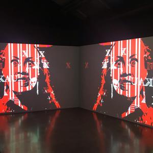 Jamies Berry Installation view of double-channel video work featuring black and red figure with the text “RAKAU” overlaid.