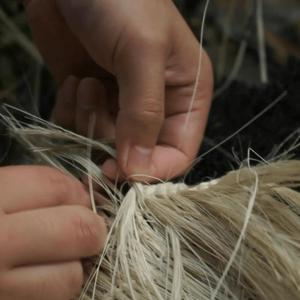 A close up of two hands weaving flax