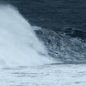 A still from Alex Monteith’s video work shows a large wave breaking. The ocean is a dark blue and foamy white.