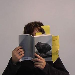 Christina is reading, holding a book which spills with bookmarks, very close to their face