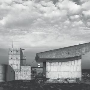 A black and white image of a concrete building with a sloped roof.