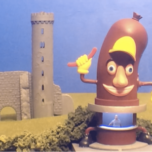 A model showing a small castle in the background and a giant sausage in the foreground with a person standing inside.