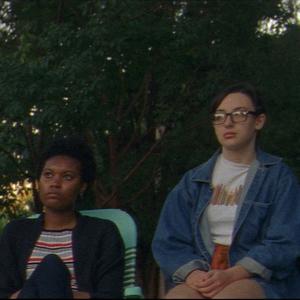 Four teenagers sit on the footpath in a row in deckchairs, gazing out into the distance.