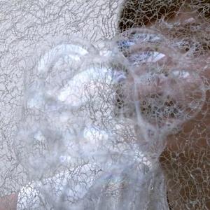 A person blows bubbles through mesh fabric.