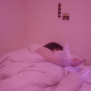 A person lies in bed while using their phone and laptop, the room is all pink.