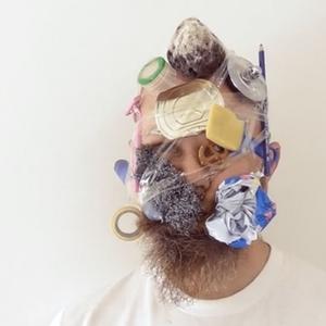 Bryce Galloway has taped household objects to his head in this till of his work. A pencil, lid of a tin can, pretzel, compressed redbull can, cheese and a rock are held to his head with a roll of tape.