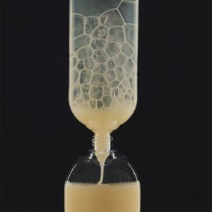A large upturned bottle of pale yellow hand wash gradually empties its contents into another bottle.
