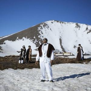 In this still of Christopher Ulutupu's video work the artist's father stands on a sunny, snowy mountain peak wearing a dapper white suit, sunglasses and fur throw, looking up towards the sun shining. The artist’s mother and sisters are in the background all wearing glamorous clothing in the bright snow