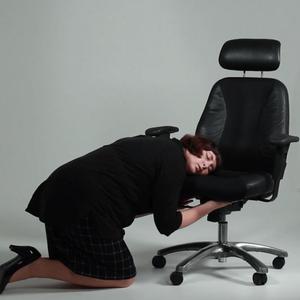 Claire wears a pencil skirt, blazer and high heels whilst tenderly hugging an office chair, resting her face against the seat