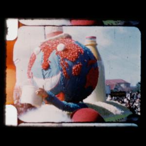 A person wearing a hand made earth costume holds a bucket up in this scanned film negative