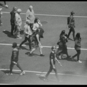 A grainy black and white image of pedestrians crossing an intersection.