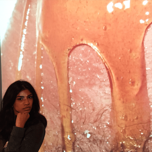 Dilohana sits with her hand on her chin, looking serious, in front of a projection of her video work.