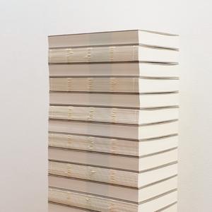 A tall stack of books that have their spines removed sits neatly in front of a white wall