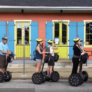 A small tour group of people on electric segways are assembled in front of a brightly coloured cafe in the Tremé district of New Orleans.