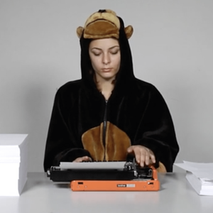 A person wearing a monkey onesie types on a orange type writer.