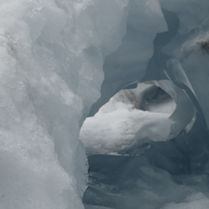 A white and pale blue ice cave holds fragments of dirt and smooth heavy ice.