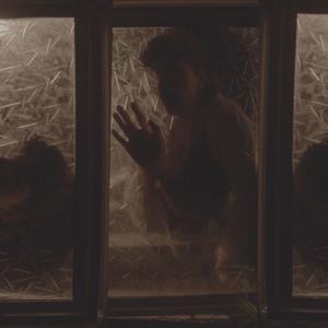 Behind three panels of frosted glass we see three separate shots of the same person with their hand pressed to the glass. Their face is in shadow.