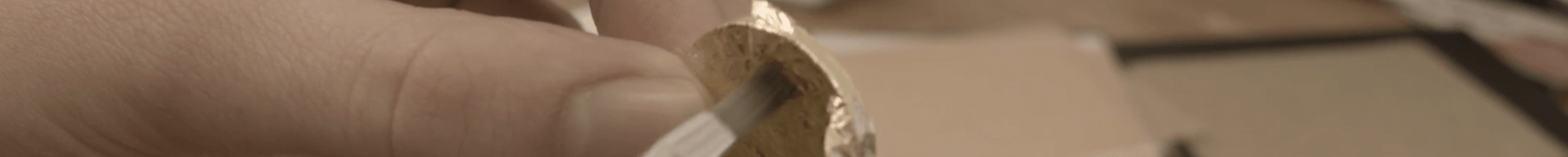Gold leaf is being pushed lightly by a paintbrush onto a coin shape making counterfeit gold coin