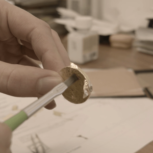 Gold leaf is being pushed lightly by a paintbrush onto a coin shape making counterfeit gold coin