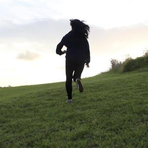 A black silhouette of a person running towards the top of a hill in late afternoon pale winter light.