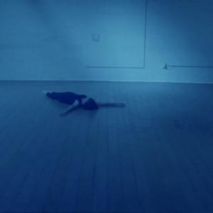 In a blue light, a dancer lies on the floor of a dance studio