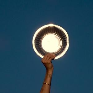 A hand holds a gold charger plate up against a bright blue sky