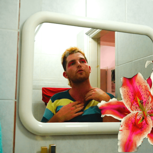 ZK gazes at themselves in a rounded mirror, they are wearing pink eye shadow and a striped top. Overlaid over the image are two large pink flowers