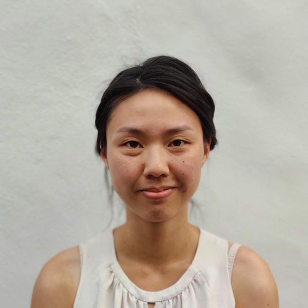 A person standing in front of a white backdrop with dark hair.