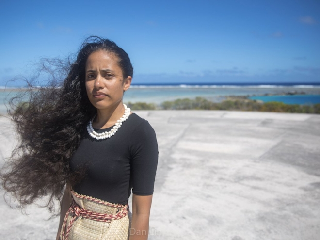 With a serious expression, Kathy looks to the camera with a tense feeling of desperation. Their hair blows in the wind and they stand on a large concrete floor near the beach