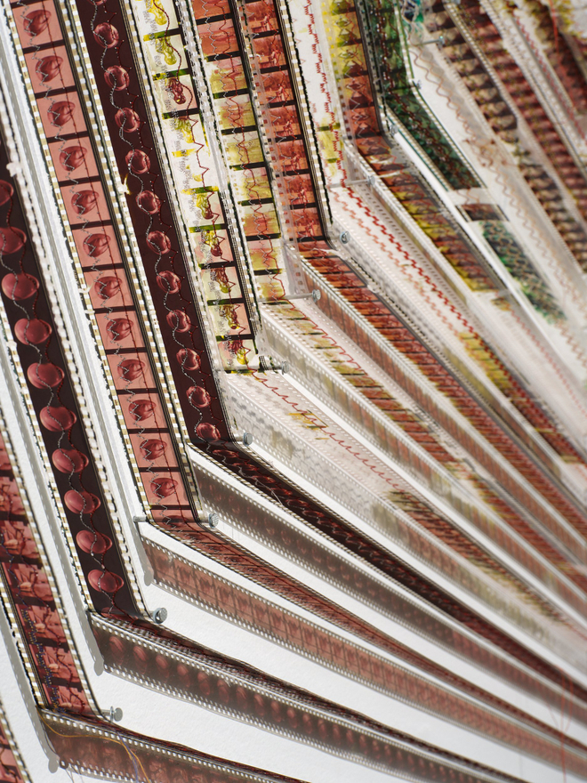 A detail of the repeating frames of a moving image film roll, spiralled on a wall
