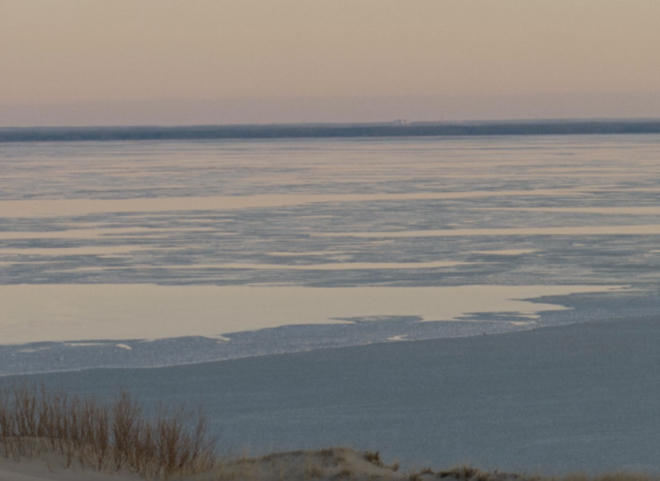 An image of a body of water at low tide, with a horizon showing a single building on a wide, thin crop of land.