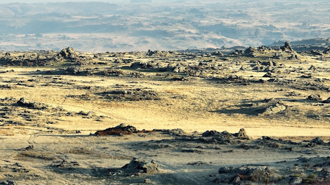 View of an arid rocky landscape shot from a drone. Fencing and tussock are visible