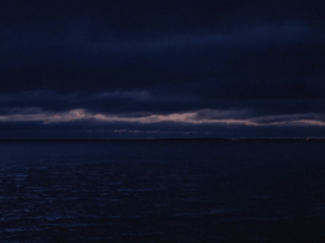 A seascape at dusk, with the last light of the day appearing between cloud.