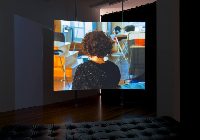 An image of the back of a person, showing their dark curly hair and black top. Behind them are chairs, stairs and other functional furniture.