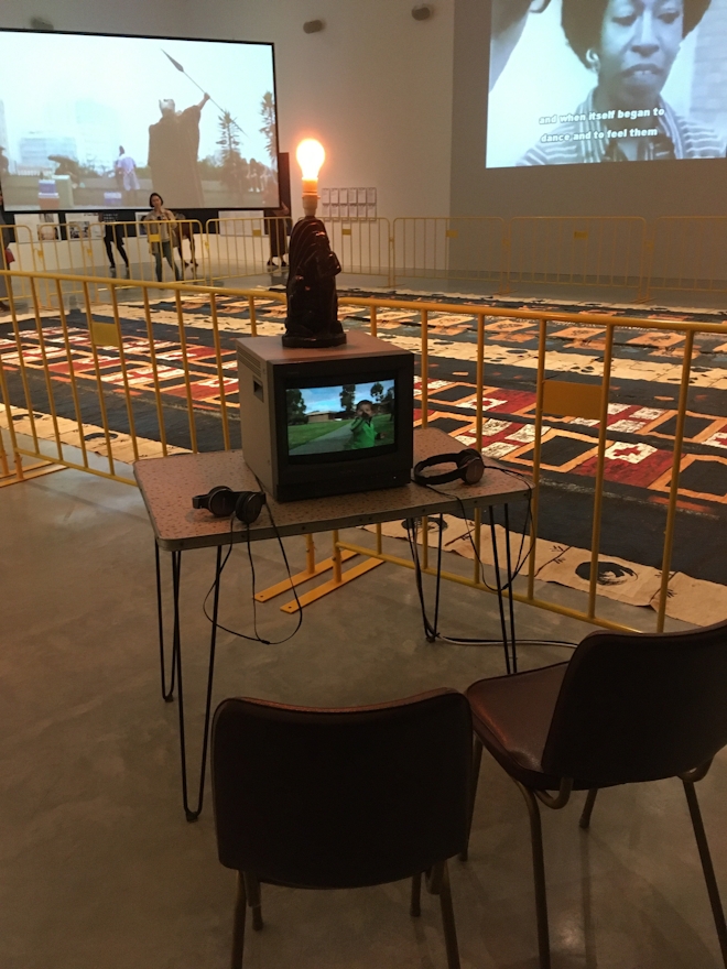 A small box tv sit on adesk in a gallery with two chairs for audiences to sit on