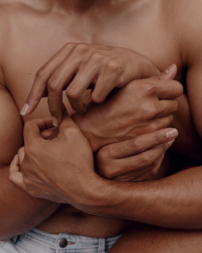 A close up of four hands embracing tenderly over a shirtless body.