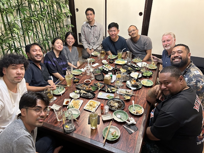 A group of people seated around a table at a Japanese restaurant. the table is covered in empty dishes, everyone is happy.