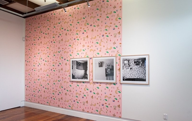 Three framed photographs on a wall that is two thirds covered with pink patterned wallpaper
