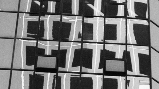 A black and white film still of reflections in the windows of a high-rise building