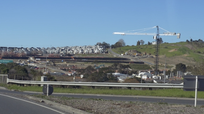 A large crane looms over a suburban, motorway-side housing development