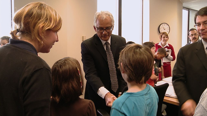 A man in a suit shakes hands with two children.